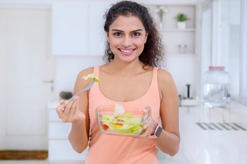 Woman eating a healthy salad after a good workout wearing a smartwatch and smiling into the camera