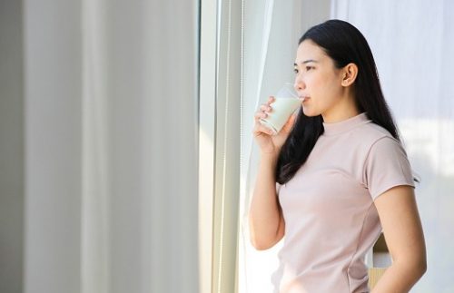 Woman drinking milk for calcium while staring outside, relaxed